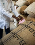 Person in a white coat interacting with coffee sacks labeled 'Coffee' in a warehouse setting.