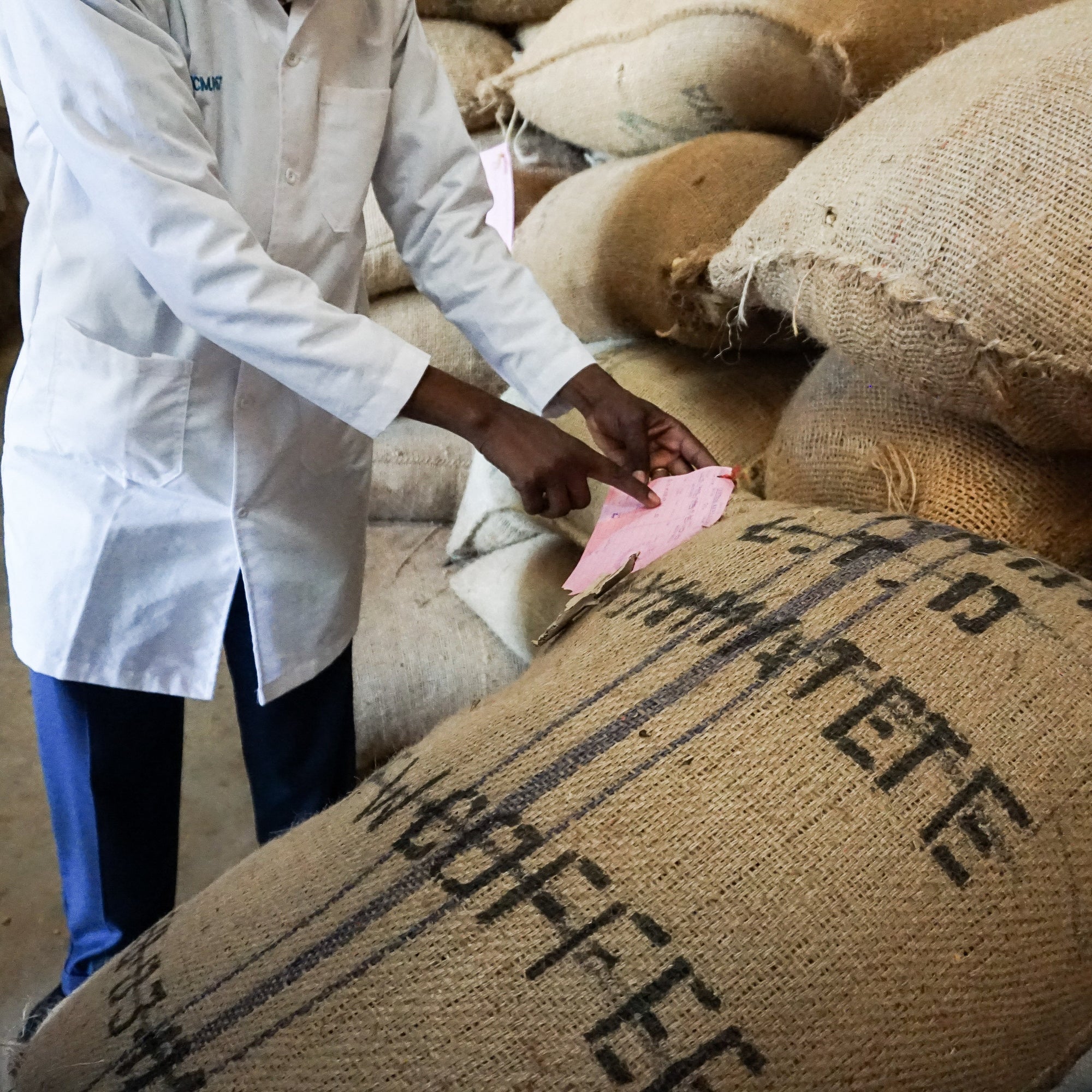 Person in a white coat interacting with coffee sacks labeled 'Coffee' in a warehouse setting.
