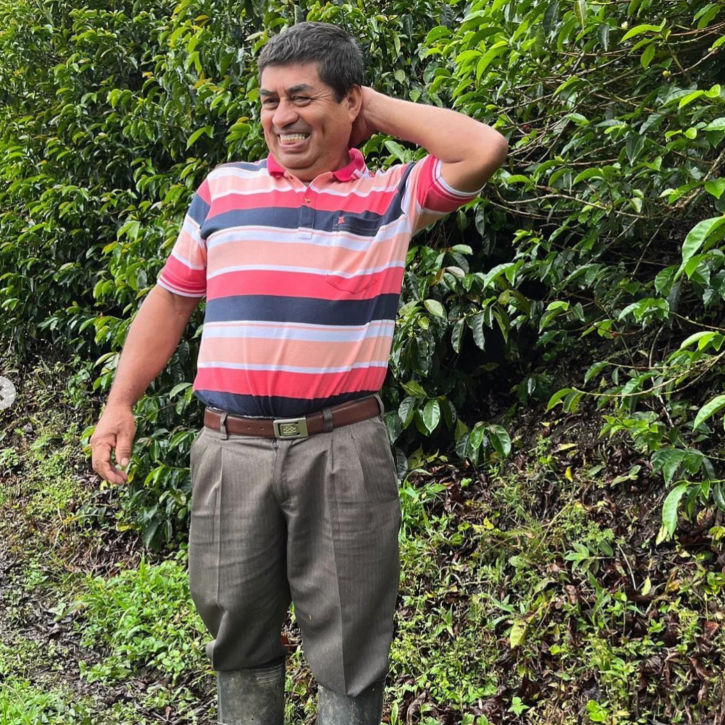 Man in a striped shirt standing in a green, leafy outdoor setting